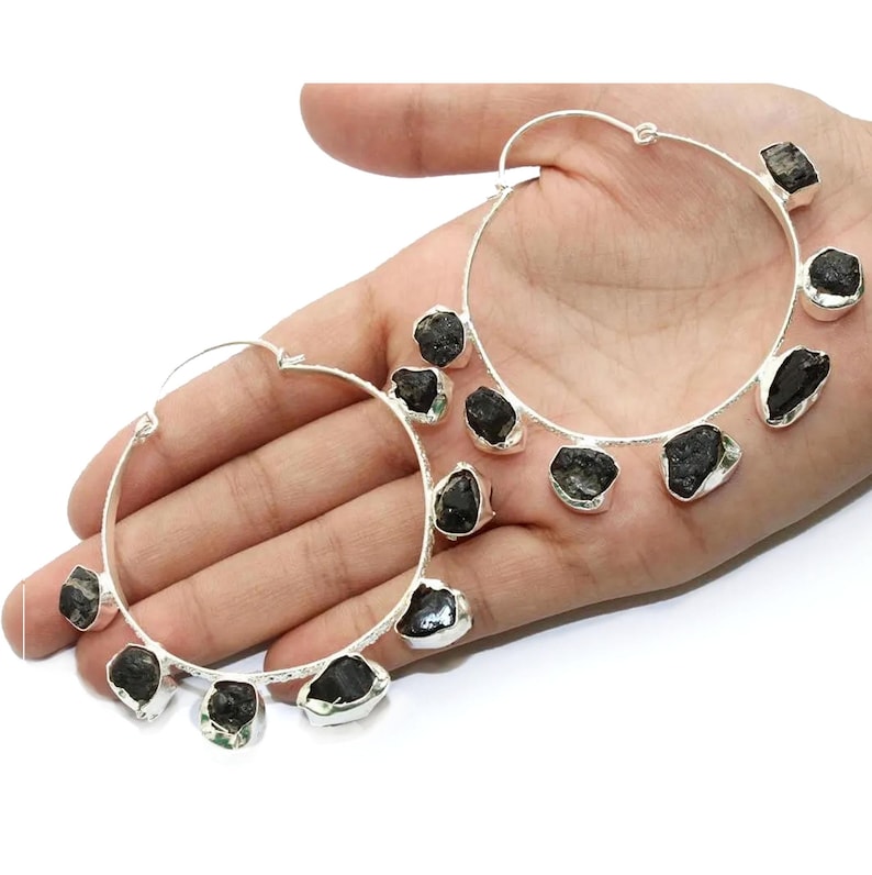 May include: Silver hoop earrings with black gemstone accents. The earrings are large and have a modern, minimalist design.