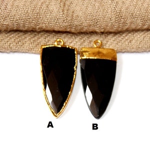 May include: Two black gemstone pendants with gold-colored trim. The pendants are teardrop-shaped with a faceted surface. Each pendant has a small loop at the top for hanging. The pendants are labeled A and B.