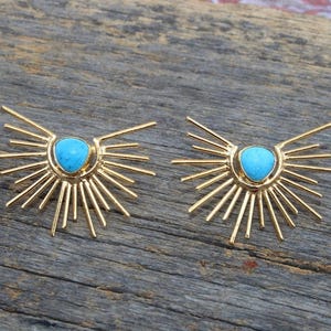 Puede incluir: Un par de pendientes de oro con piedras turquesa en el centro. Cada pendiente tiene un diseño de sol radiante con múltiples rayos que emanan del centro.