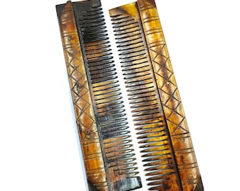 May include: Two wooden combs with detailed geometric carvings. The combs are a warm brown colour with darker accents, and the teeth are finely spaced. The handles feature a diamond pattern and small decorative details. The combs are displayed against a white background.
