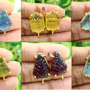 May include: Six pairs of gold-plated earring findings with carved gemstone tops. The gemstones are in various colors, including blue, yellow, green, and red.