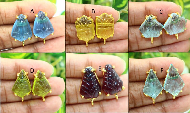 May include: Six pairs of gold-plated earring findings with carved gemstone tops. The gemstones are in various colors, including blue, yellow, green, and red.