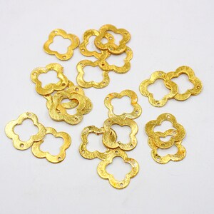 May include: A collection of gold-colored metal flower-shaped charms with a textured surface. The charms have a four-leaf clover design.
