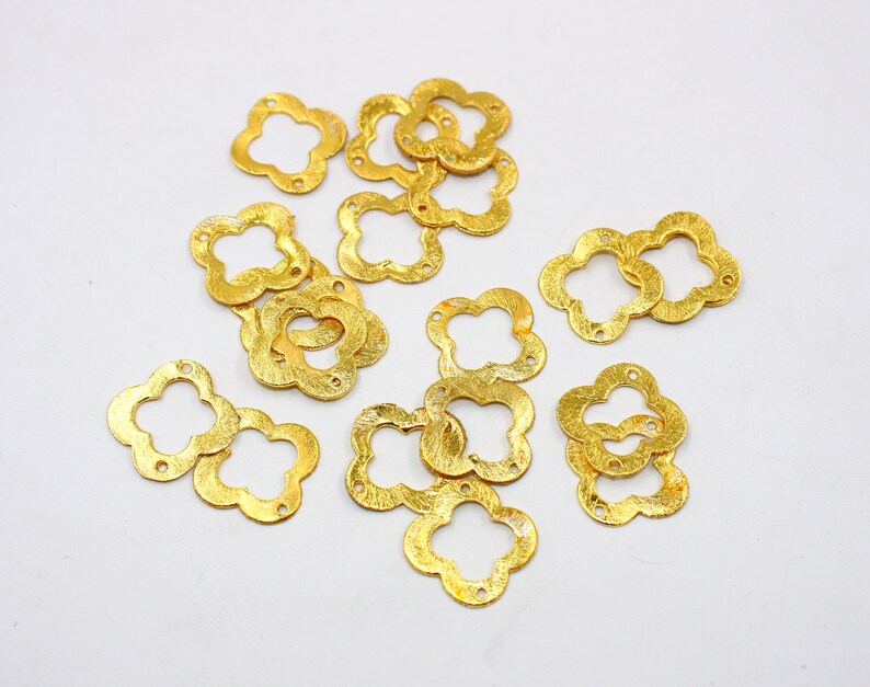 May include: A collection of gold-colored metal flower-shaped charms with a textured surface. The charms have a four-leaf clover design.