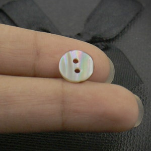 May include: A white iridescent button with two holes. The button is made of mother of pearl.