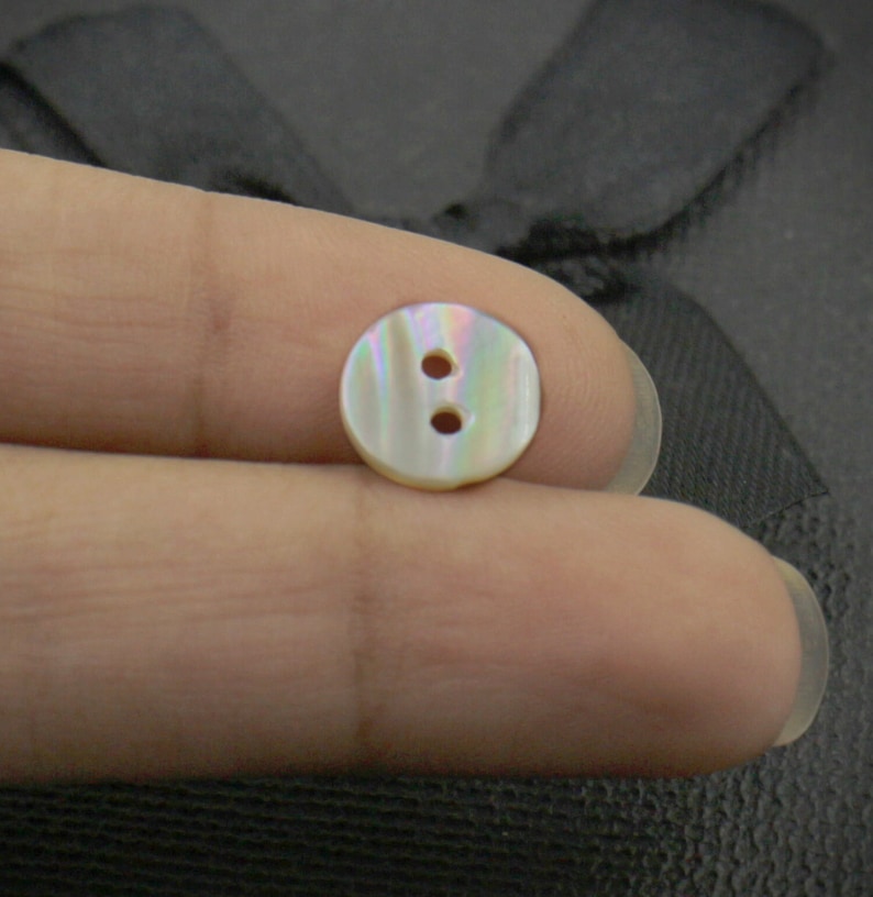 May include: A white iridescent button with two holes. The button is made of mother of pearl.