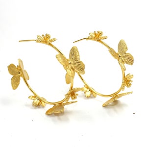 Puede incluir: Aretes de aro dorados con un delicado dise&ntilde;o de mariposa y flores. Los aretes est&aacute;n hechos de metal y tienen un acabado pulido.