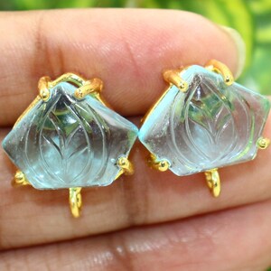 May include: A pair of gold earrings with blue carved gemstone accents. The gemstones are shaped like a flower with a carved leaf design.
