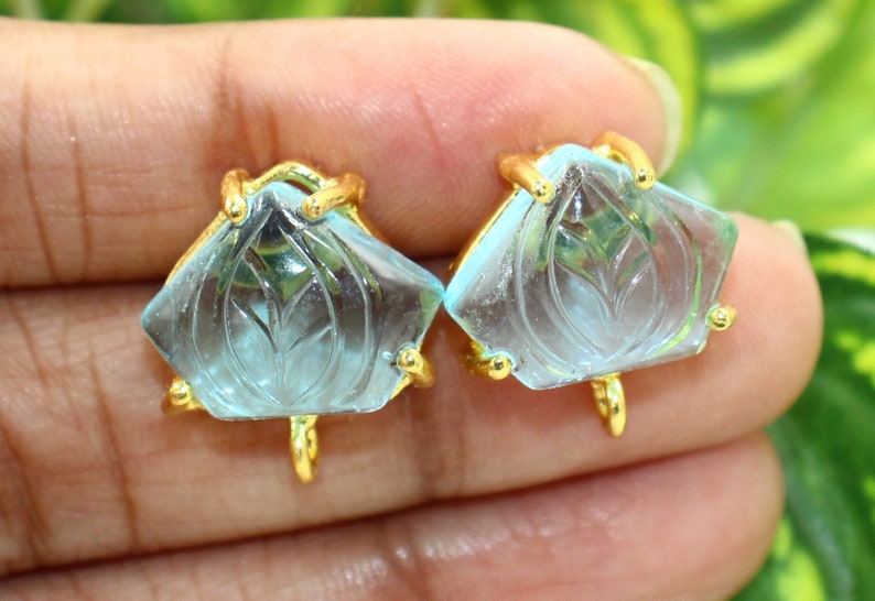 May include: A pair of gold earrings with blue carved gemstone accents. The gemstones are shaped like a flower with a carved leaf design.