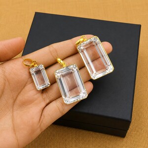 May include: Three clear rectangular pendants with gold-coloured frames and loops. The pendants are displayed on a black box, showcasing their clarity and design. The pendants vary in size, offering a set of options.
