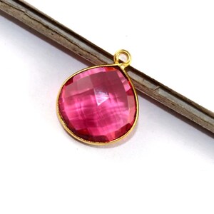 May include: A pink faceted gemstone pendant with a gold-plated bail. The pendant is shaped like a teardrop and has a shiny, polished finish.