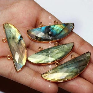 May include: Four gold-plated labradorite gemstone pendants with a half-moon shape. Each pendant has two jump rings for attaching to jewelry.