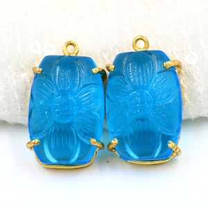 Könnte beinhalten: Zwei blaue Glas-Anhänger in Blumenform mit goldfarbenen Metallrahmen. Die Anhänger sind rechteckig und haben ein Blumenmuster.