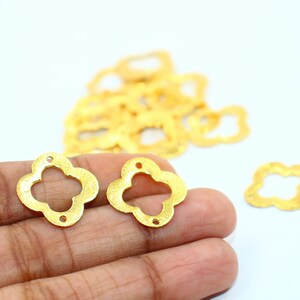 May include: Two gold-colored metal flower-shaped charms with a four-leaf clover design. The charms have a textured surface and are about 1 inch in diameter.