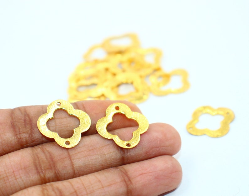 May include: Two gold-colored metal flower-shaped charms with a four-leaf clover design. The charms have a textured surface and are about 1 inch in diameter.