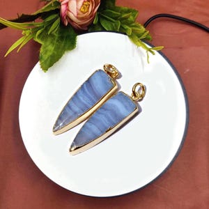 May include: Two blue agate pendants with gold-toned metal settings. The pendants are shaped like a pointed triangle.