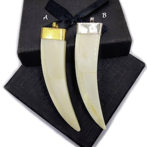 May include: Two white tooth-shaped pendants with gold and silver accents. The pendants are displayed on a black background with the letters A and B.