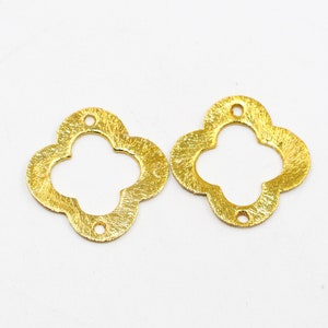 May include: Two gold-colored metal clover-shaped charms with a textured finish. Each charm has a hole in the center for attaching to jewelry or other crafts.