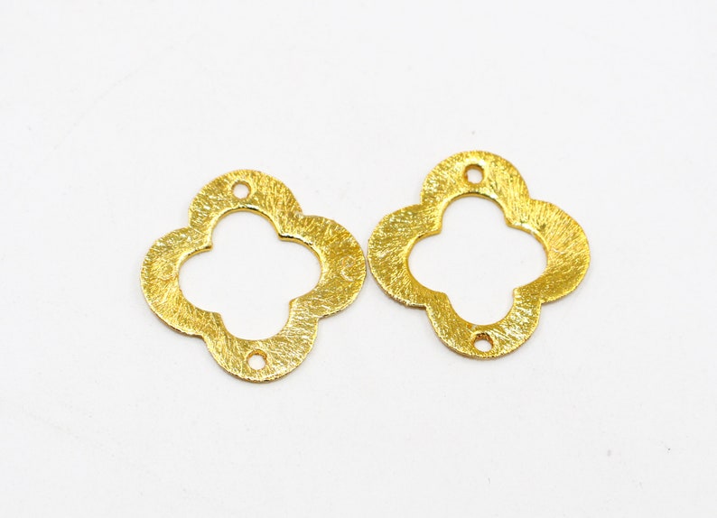 May include: Two gold-colored metal clover-shaped charms with a textured finish. Each charm has a hole in the center for attaching to jewelry or other crafts.