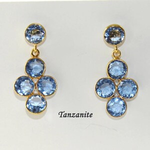 May include: A pair of gold dangle earrings with blue Tanzanite gemstones. The earrings feature a cluster of five round stones.