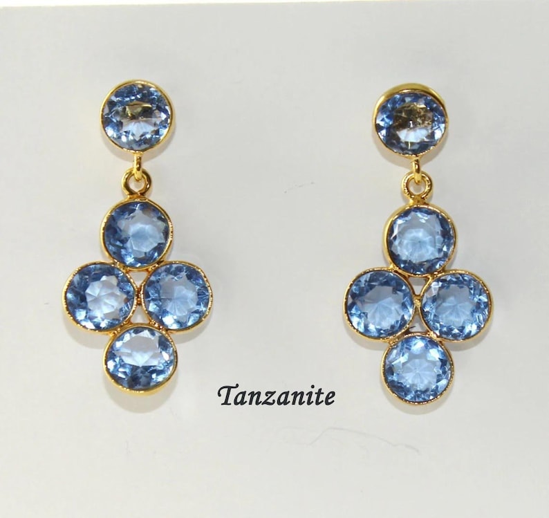 May include: A pair of gold dangle earrings with blue Tanzanite gemstones. The earrings feature a cluster of five round stones.