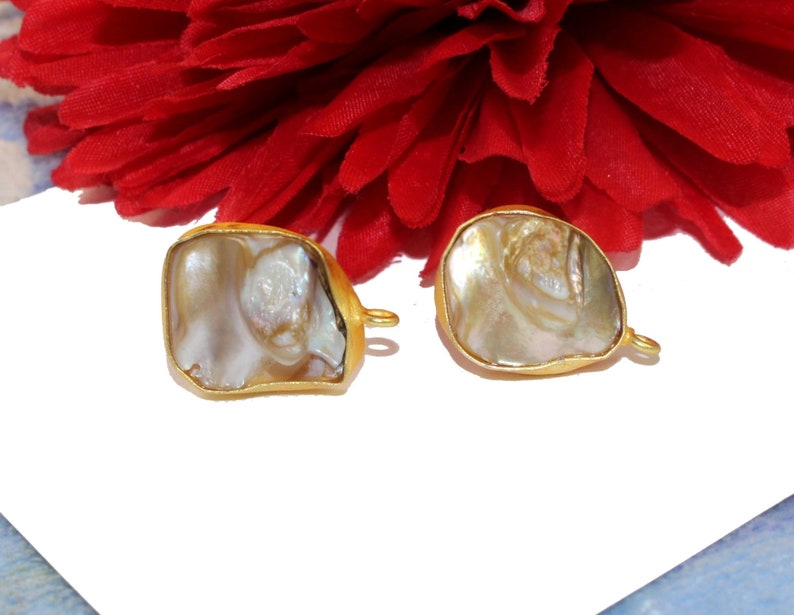 May include: Two gold-toned metal charms with a white iridescent shell inlay. The charms have a loop on the side for attaching to jewelry.