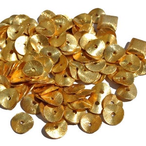 May include: A large pile of gold-colored metal sequins, each with a small hole in the center. The sequins are scattered on a white background.