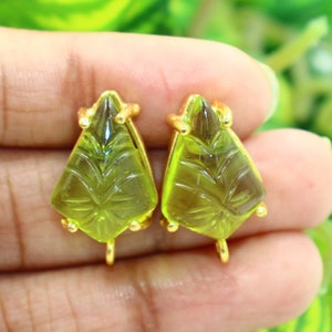 May include: A pair of gold-tone earrings with green glass teardrop-shaped stones. The stones have a carved design and are set in a gold-tone metal.