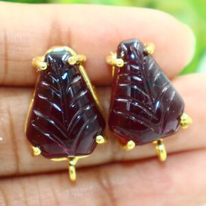 May include: A pair of red gemstone earrings with gold accents. The gemstones are carved with a leaf design.