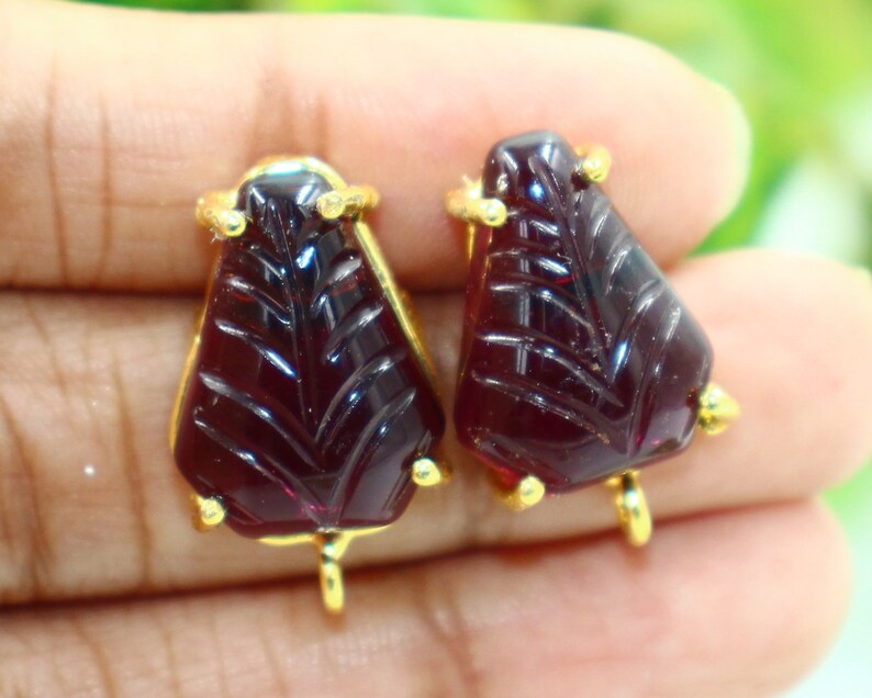 May include: A pair of red gemstone earrings with gold accents. The gemstones are carved with a leaf design.