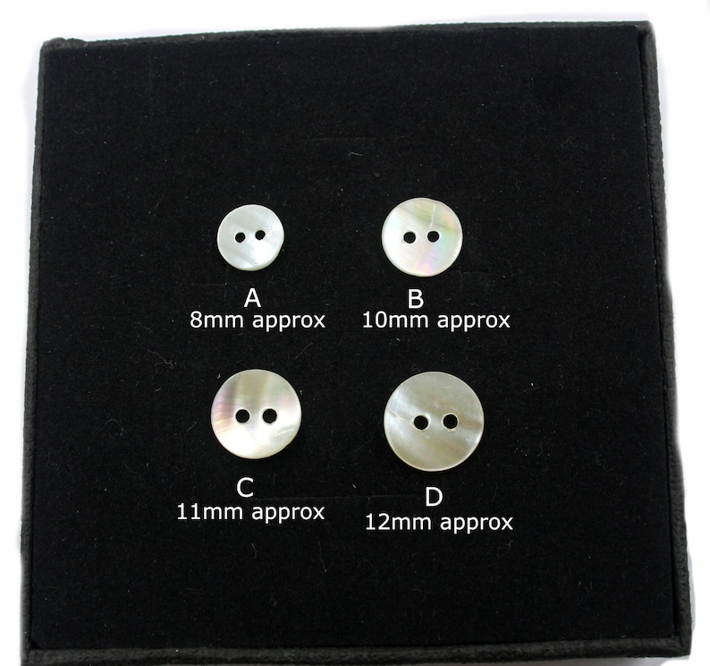 May include: Four white mother of pearl buttons with two holes each, displayed on a black background. The buttons are labeled A, B, C, and D, with approximate measurements in millimeters.