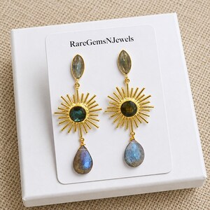 Puede incluir: Pendientes colgantes dorados con dise&ntilde;o de rayos de sol, una piedra central oscura, una piedra superior en forma de marquesa y un colgante de labradorita en forma de l&aacute;grima. Presentados en una tarjeta blanca con el texto RareGemsNJewels.