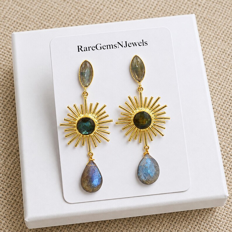 Puede incluir: Pendientes colgantes dorados con dise&ntilde;o de rayos de sol, una piedra central oscura, una piedra superior en forma de marquesa y un colgante de labradorita en forma de l&aacute;grima. Presentados en una tarjeta blanca con el texto RareGemsNJewels.