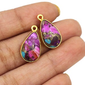 Puede incluir: Dos colgantes en forma de lágrima chapados en oro con una piedra colorida, veteada e iridiscente. La piedra tiene tonos de rosa, morado, turquesa y dorado.