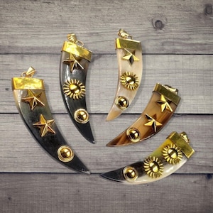 May include: Four horn-shaped pendants with gold-colored accents. Each pendant features a gold-colored cap and decorative elements, including stars, suns, and circular studs. The horns vary in color, ranging from dark grey to light brown.