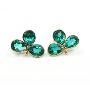 May include: A pair of gold earrings with three green clover-shaped stones.