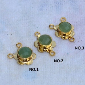 May include: Three gold-tone metal connector charms with green gemstone accents. Each charm has a flower-shaped design with three loops for attaching jewelry.