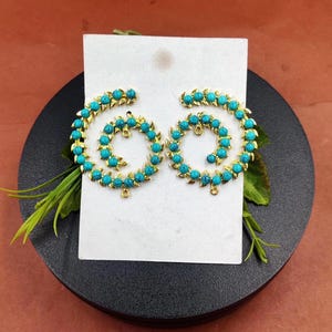 Puede incluir: Un par de pendientes de oro con cuentas de color azul turquesa dispuestas en espiral.
