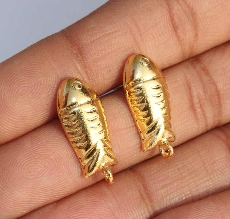 May include: Two gold-colored fish charms with a textured surface. The charms have a loop at the bottom for attaching to jewelry or other crafts.