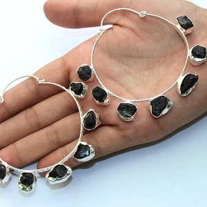 May include: A pair of silver hoop earrings with black gemstone accents. Each earring has five black gemstones dangling from the hoop.