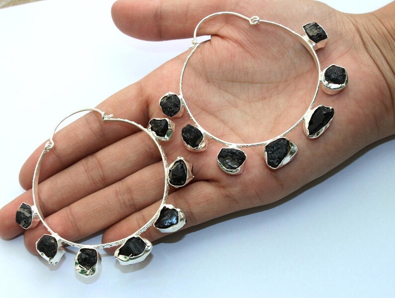 May include: A pair of silver hoop earrings with black gemstone accents. Each earring has five black gemstones dangling from the hoop.