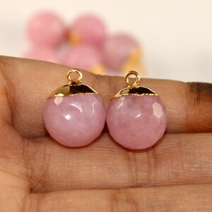 Puede incluir: Dos colgantes de piedra rosa con detalles dorados. Los colgantes son redondos y tienen un acabado liso y pulido.