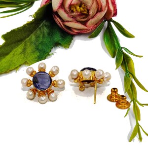 Peut inclure: Une paire de boucles d'oreilles en or avec un centre de pierre pr&eacute;cieuse bleue entour&eacute; de perles blanches. Les boucles d'oreilles ont un fermoir &agrave; tige.