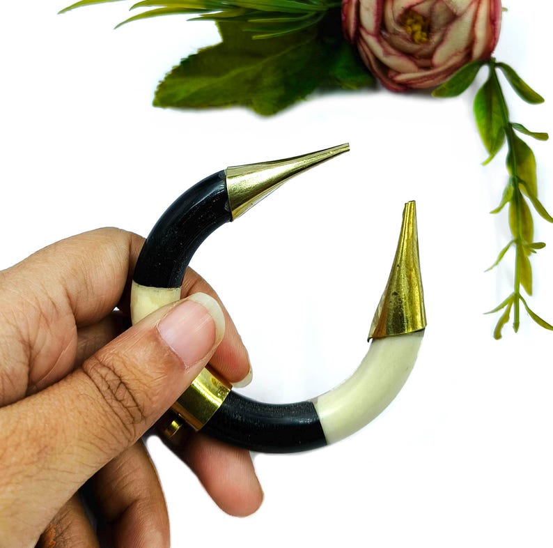 Peut inclure: Un bracelet incurv&eacute; compos&eacute; de segments altern&eacute;s en mat&eacute;riau noir et blanc cass&eacute;, agr&eacute;ment&eacute; d'embouts en m&eacute;tal dor&eacute; poli aux deux extr&eacute;mit&eacute;s et d'une pi&egrave;ce de connexion centrale en m&eacute;tal dor&eacute;, formant une forme circulaire ouverte.