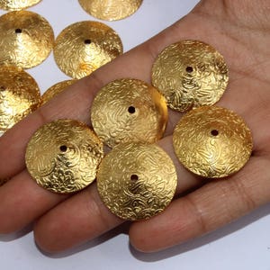 May include: A collection of gold-toned metal embellishments with a decorative floral pattern. The embellishments are round and have a small hole in the center.