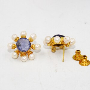 Peut inclure: Une paire de boucles d'oreilles en or avec un centre de pierre pr&eacute;cieuse bleue entour&eacute; de perles blanches. Les boucles d'oreilles ont un fermoir &agrave; tige.