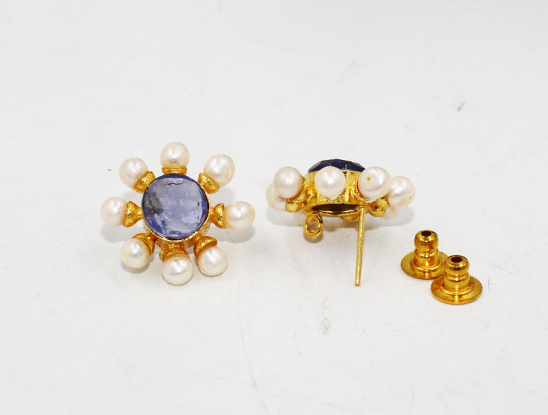 Peut inclure: Une paire de boucles d'oreilles en or avec un centre de pierre pr&eacute;cieuse bleue entour&eacute; de perles blanches. Les boucles d'oreilles ont un fermoir &agrave; tige.