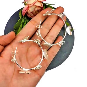 Puede incluir: Pendientes de aro de plata con abalorios de mariposa. Los pendientes son grandes y tienen un dise&ntilde;o delicado.