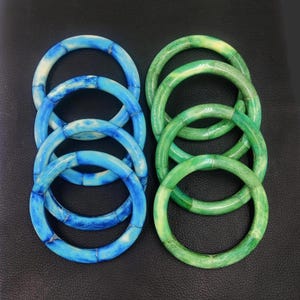 May include: Set of six bangle bracelets, three blue and three green. The bracelets are made of a material that resembles bone or shell and have a marbled pattern.