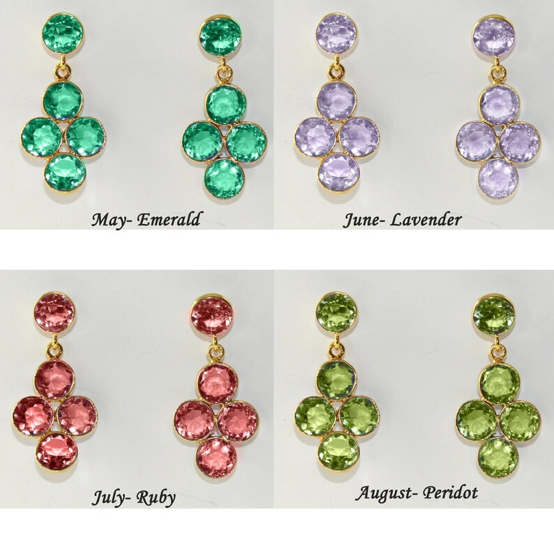 May include: Four pairs of dangle earrings with a cluster of five round gemstones. The earrings are gold-toned and feature different colored gemstones: emerald green, lavender, ruby red, and peridot green. The text below each pair of earrings identifies the birthstone month and gemstone name: May-Emerald, June-Lavender, July-Ruby, August-Peridot.